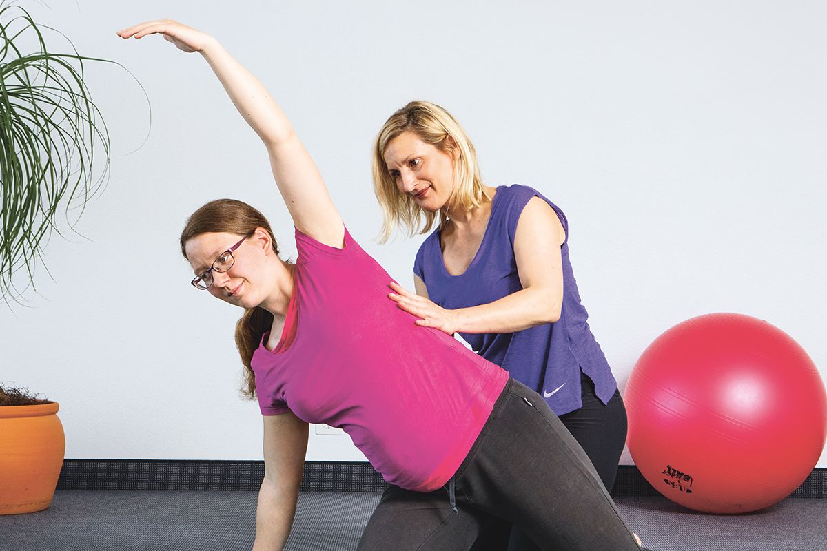 Instruktorin unterstützt eine schwangere Frau bei Pilates.