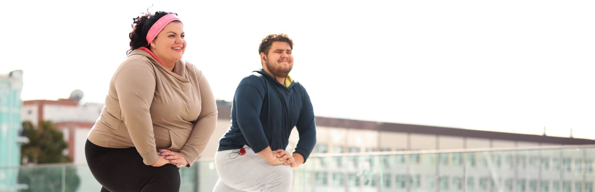 Zwei übergewichtige Personen in Sportkleidern machen Dehnübungen.