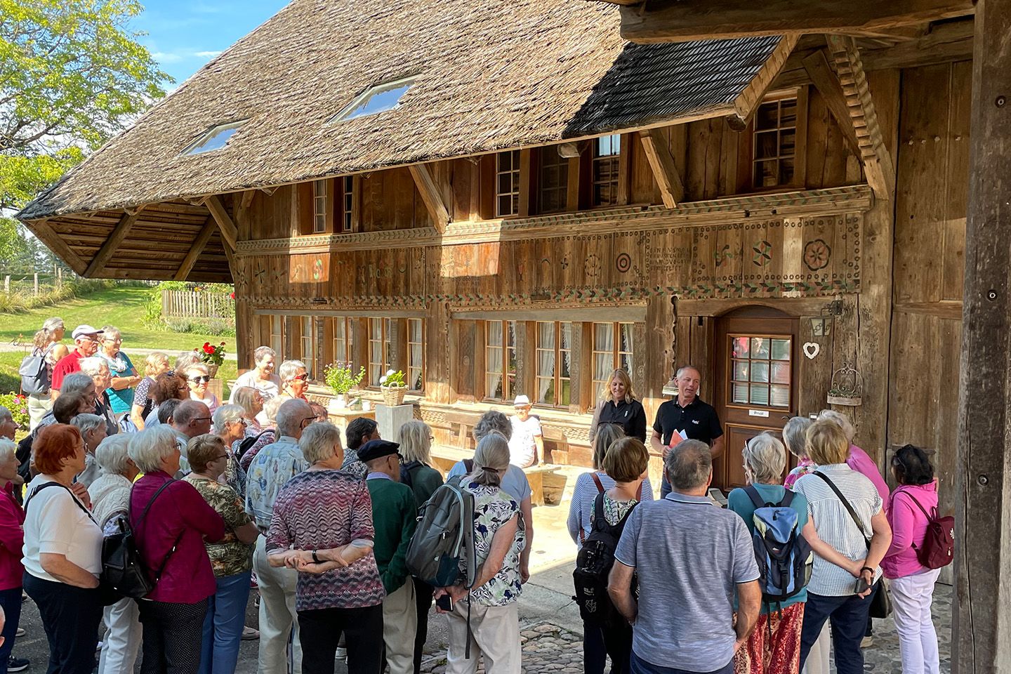 Die Reisegruppe steht vor einem bemalten Bauernhaus und lauscht den Erzählungen der Hofbesitzer.